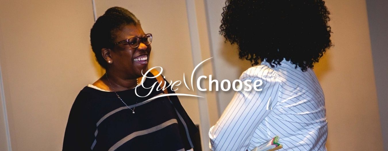 Two women smiling and talking at a community event, with “Give Choose” text and the Loudoun Coalition Women and Girls logo displayed.