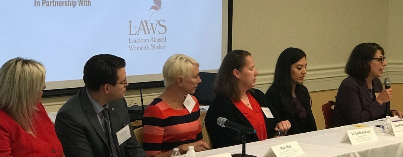 Panel discussion on ending violence against women, featuring several speakers seated at a conference table with microphones.