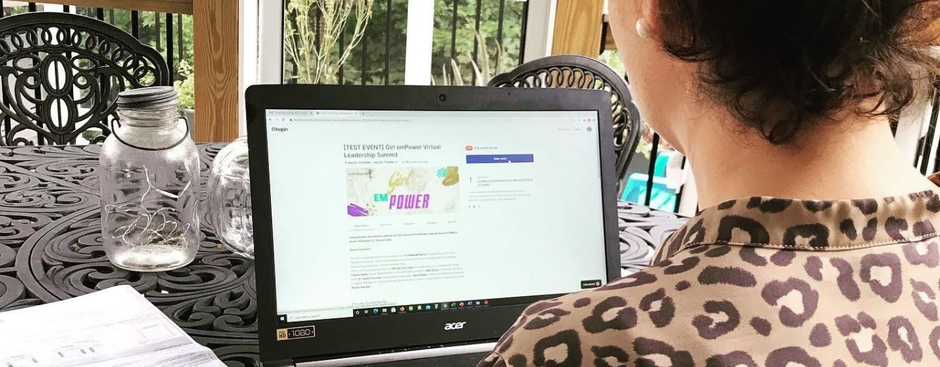 Person using a laptop to view a virtual girls’ empowerment summit registration page while seated at an outdoor table.